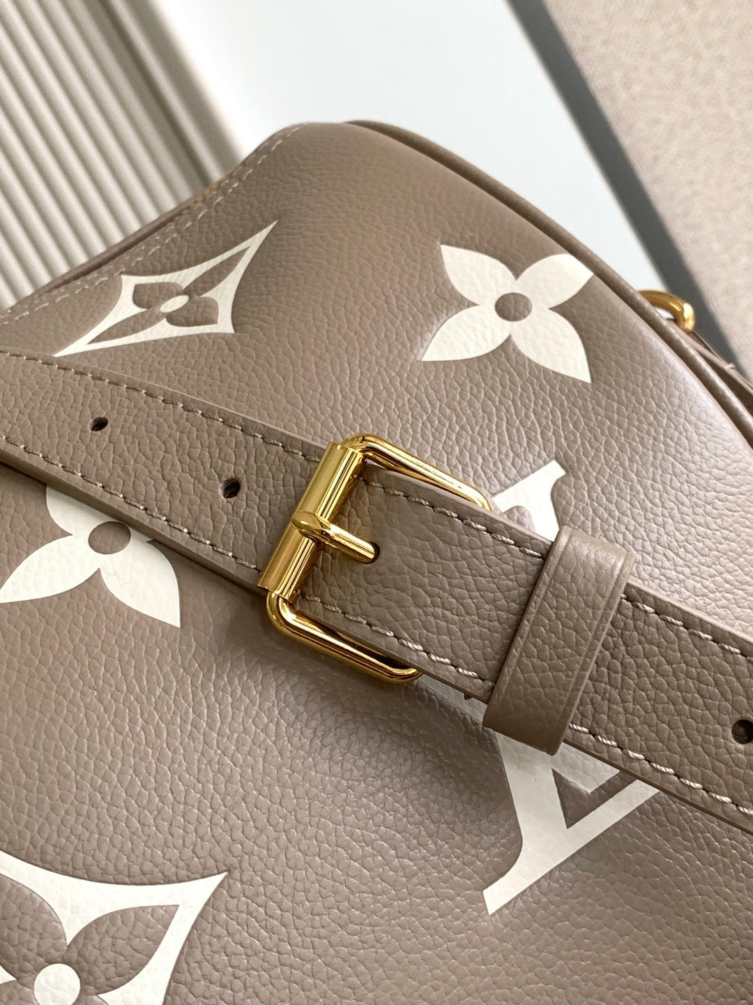 Louis Vuitton bag close-up: taupe strap with engraved gold buckle and white monogram flowers