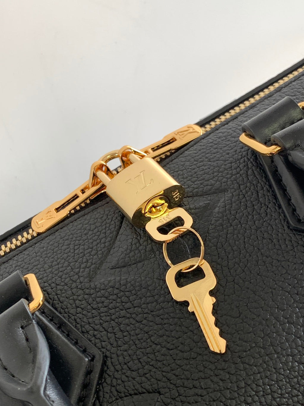 Louis Vuitton bag close-up of gold zipper pull and key-shaped charm on textured leather