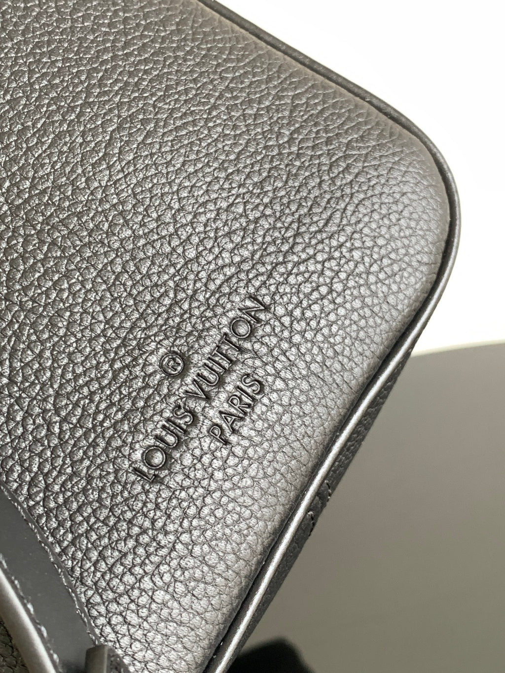 Louis Vuitton logo embossed on textured dark leather trim at bag corner