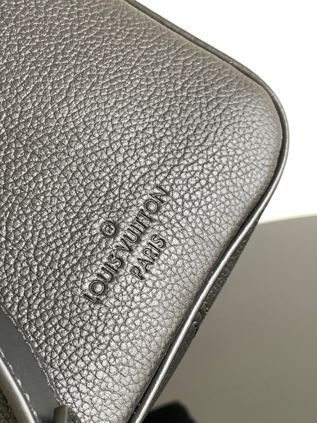Louis Vuitton logo embossed on textured dark leather trim at bag corner