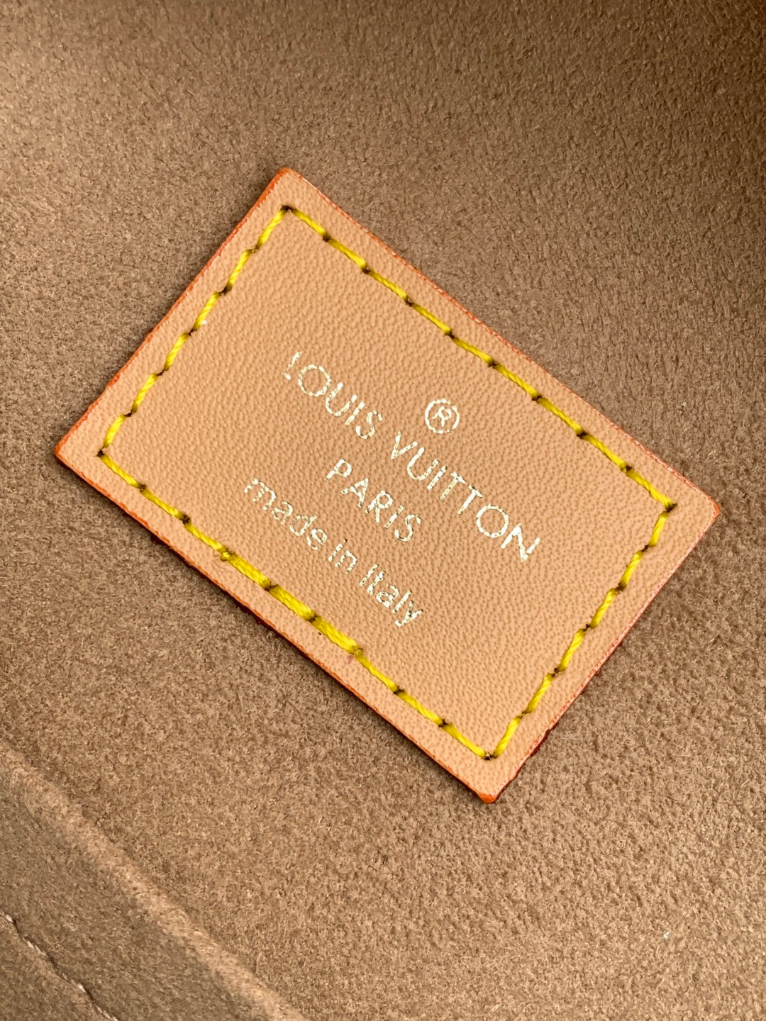 Louis Vuitton bag authenticity label on tan leather patch with yellow stitching