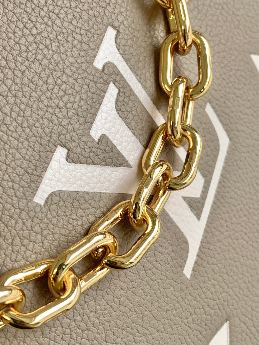 Close-up of taupe leather with embossed monogram and gold chain hardware on bag.