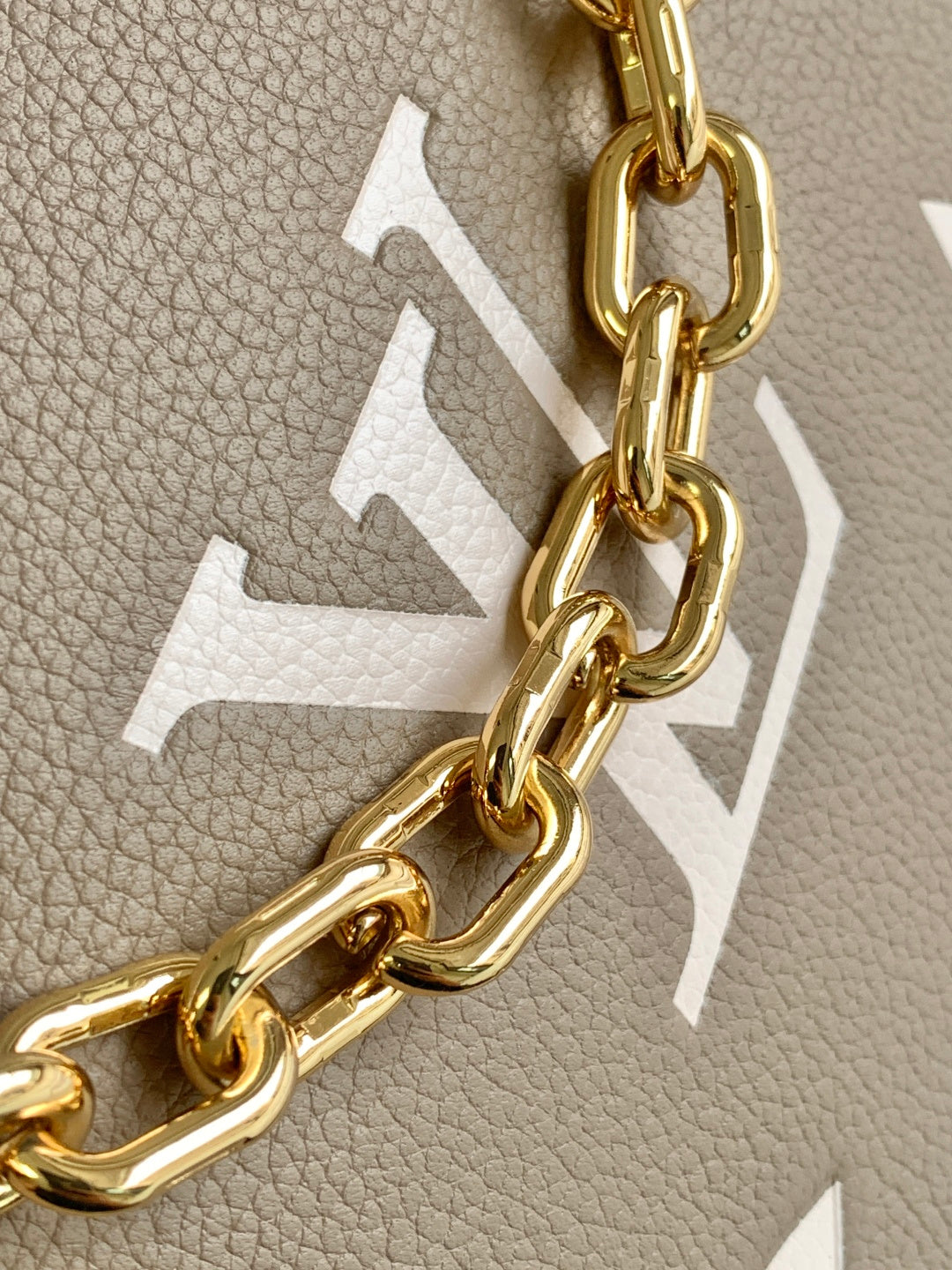 Close-up of taupe leather with embossed monogram and gold chain hardware on bag.