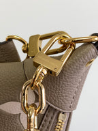 Close-up of gold strap clasp and rings on taupe monogram bag with leather details.