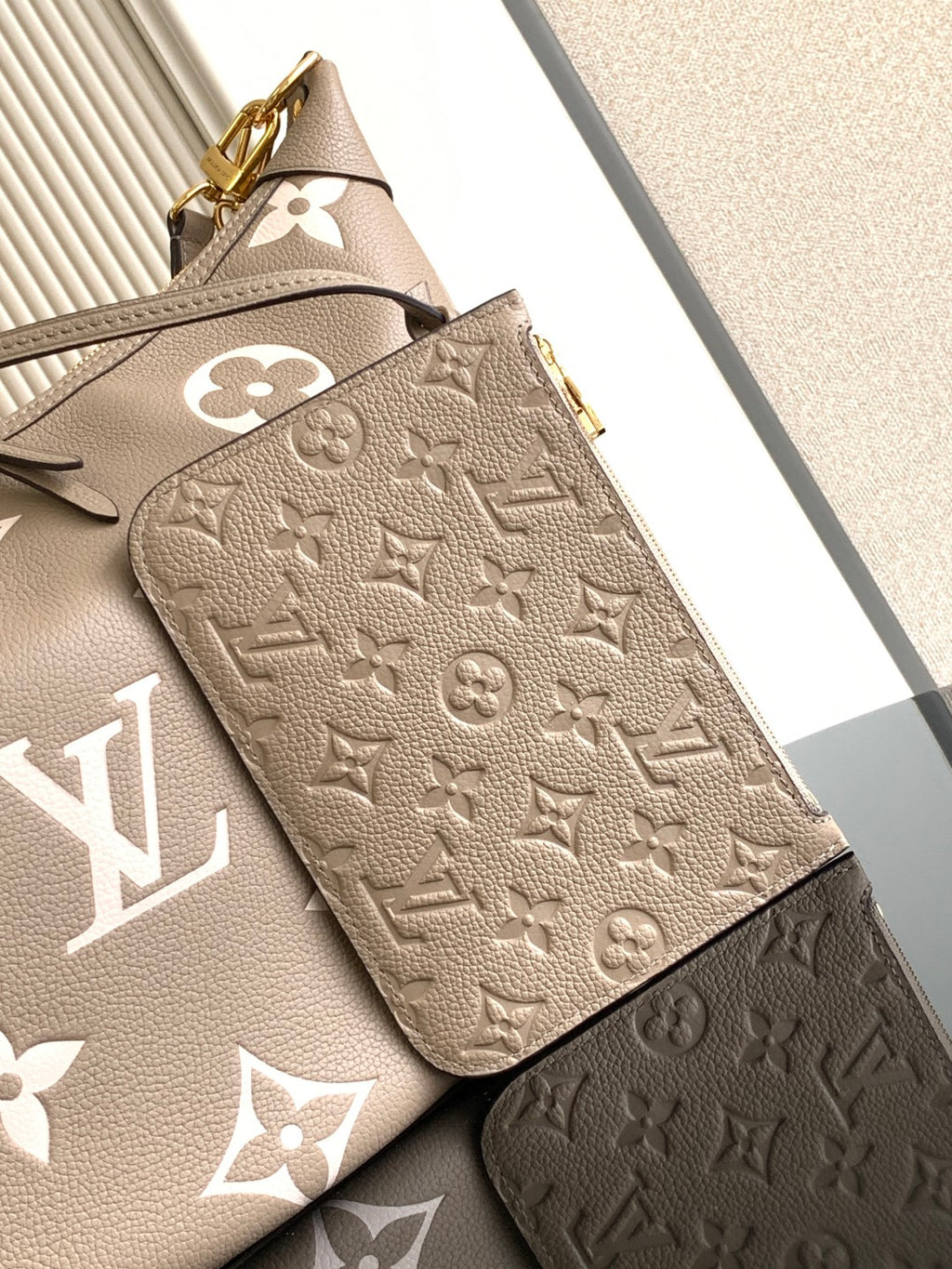 Beige monogram wallet pouch with embossed pattern and gold clasp detail on front.