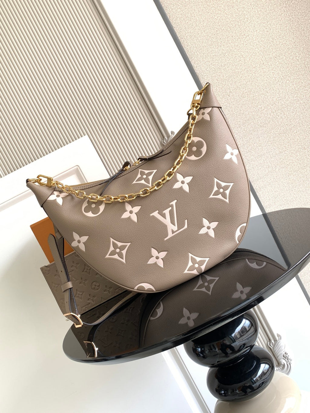 Monogram hobo bag in taupe with white pattern, gold chain strap, and zip top.