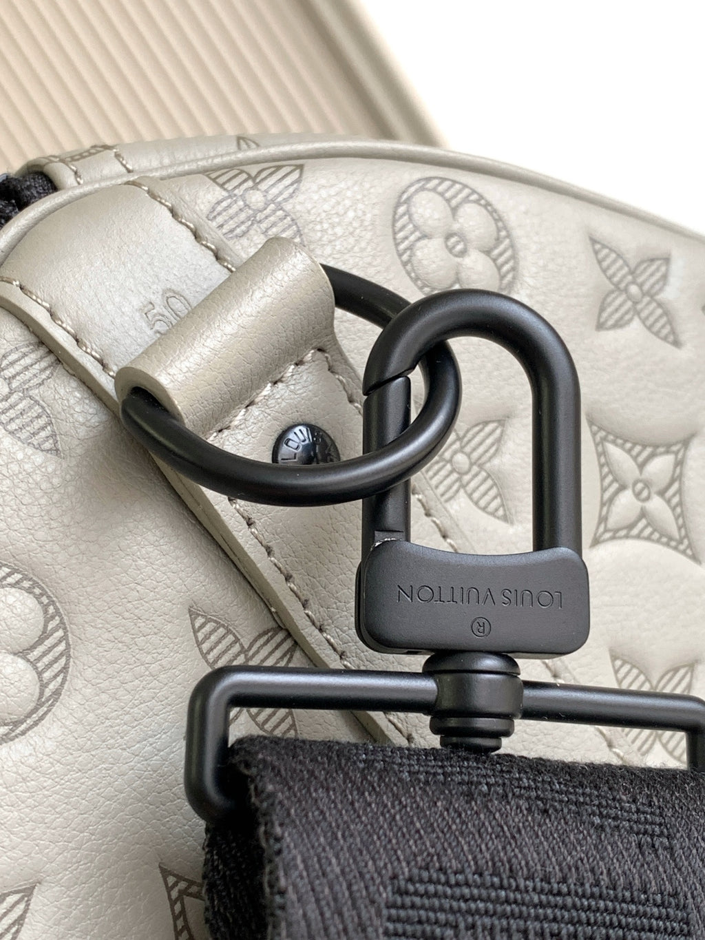 Monogram bag clasp with black O-ring and logo-engraved lock on light gray leather