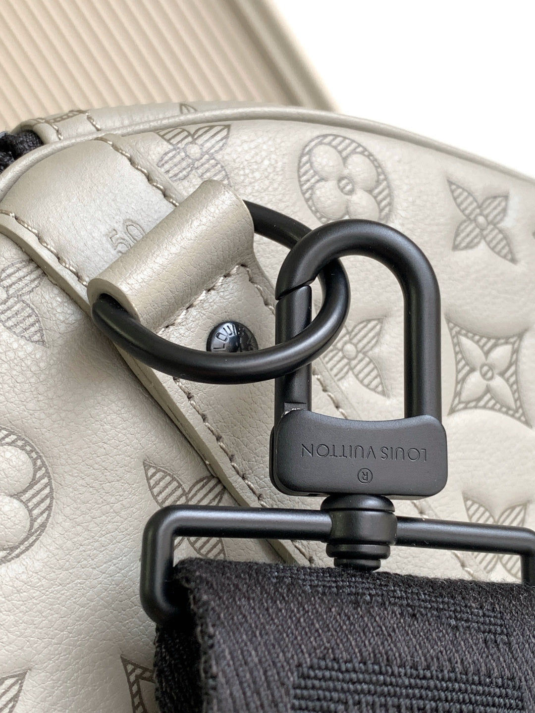 Monogram bag clasp with black O-ring and logo-engraved lock on light gray leather