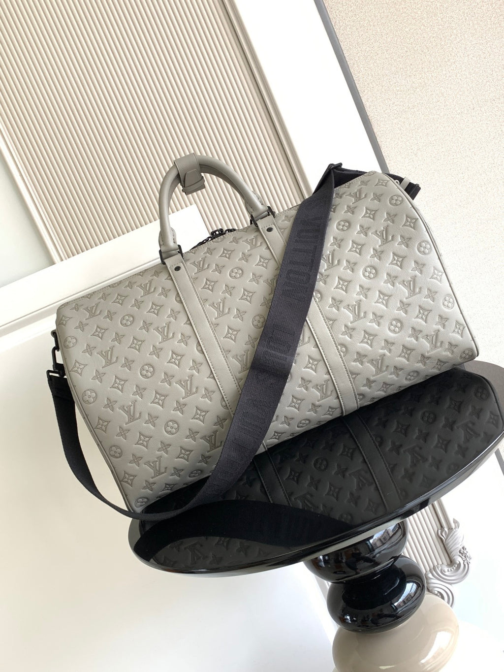 Monogram duffel bag in light gray with top handles and dark blue shoulder strap