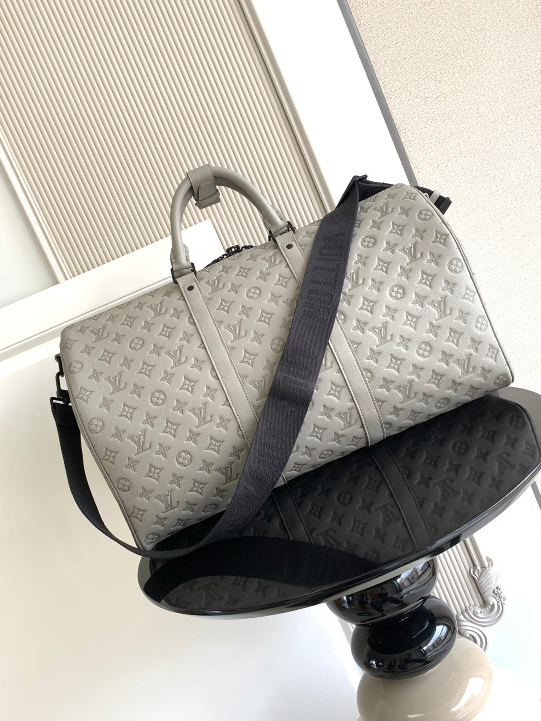 Monogram duffel bag in light gray with top handles and dark blue shoulder strap