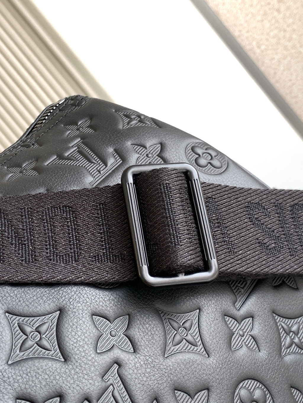 Louis Vuitton bag strap detail with silver-tone buckle on textured dark leather
