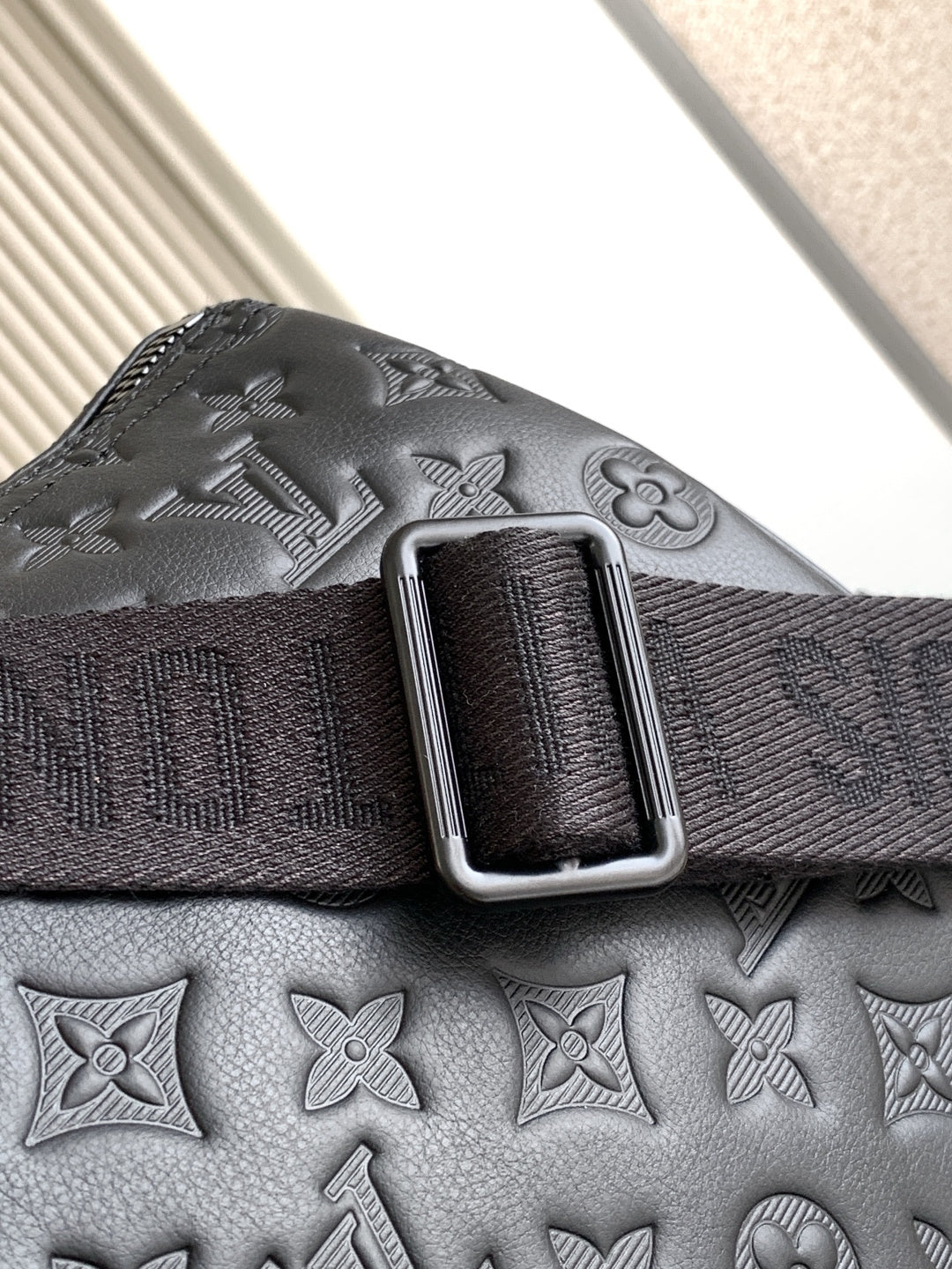Louis Vuitton bag strap detail with silver-tone buckle on textured dark leather