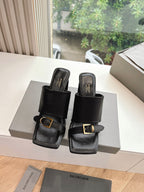 Black heeled slide sandals on display, featuring gold-tone buckle on strap