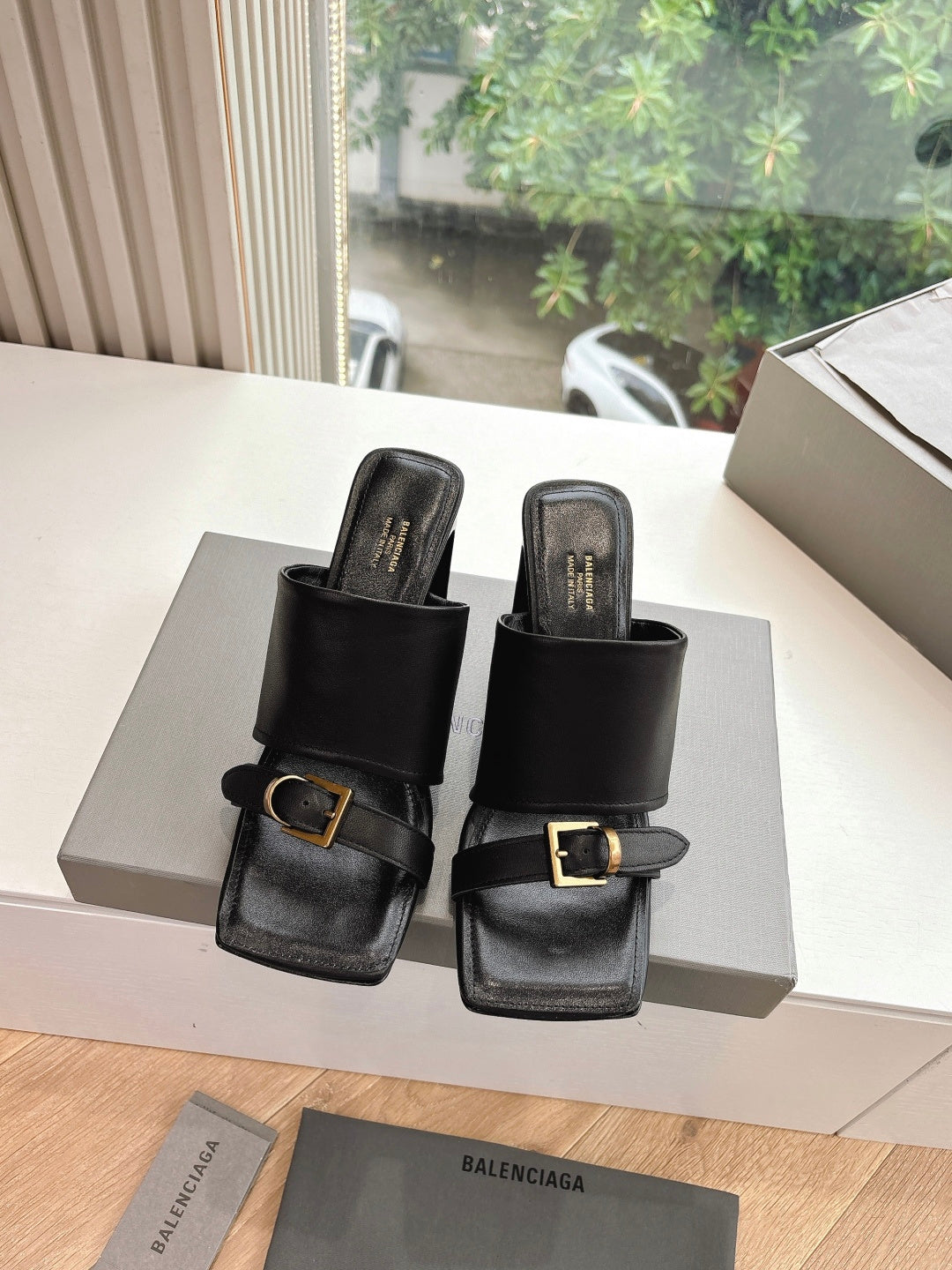 Black heeled slide sandals on display, featuring gold-tone buckle on strap