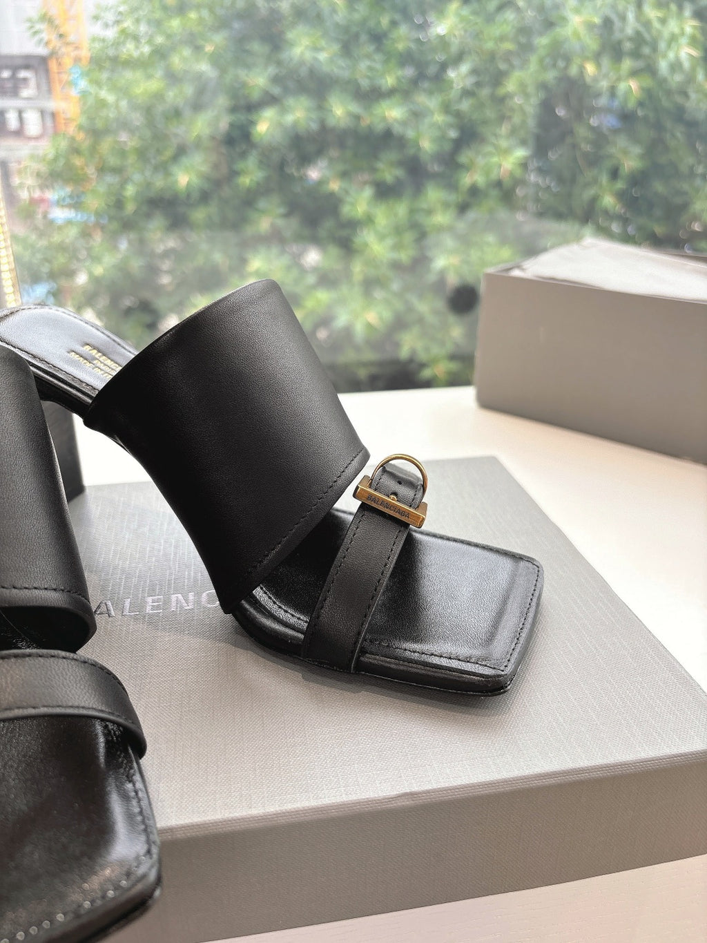 Close-up of black heeled slide sandal with gold-tone buckle and wide strap