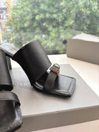 Close-up of black heeled slide sandal with gold-tone buckle and wide strap