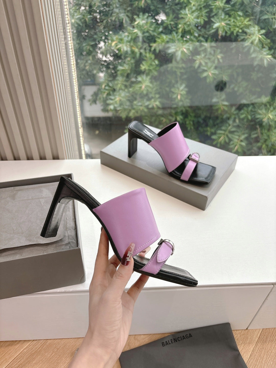Pink mule-style sandals with black toe strap and square metal buckle detail