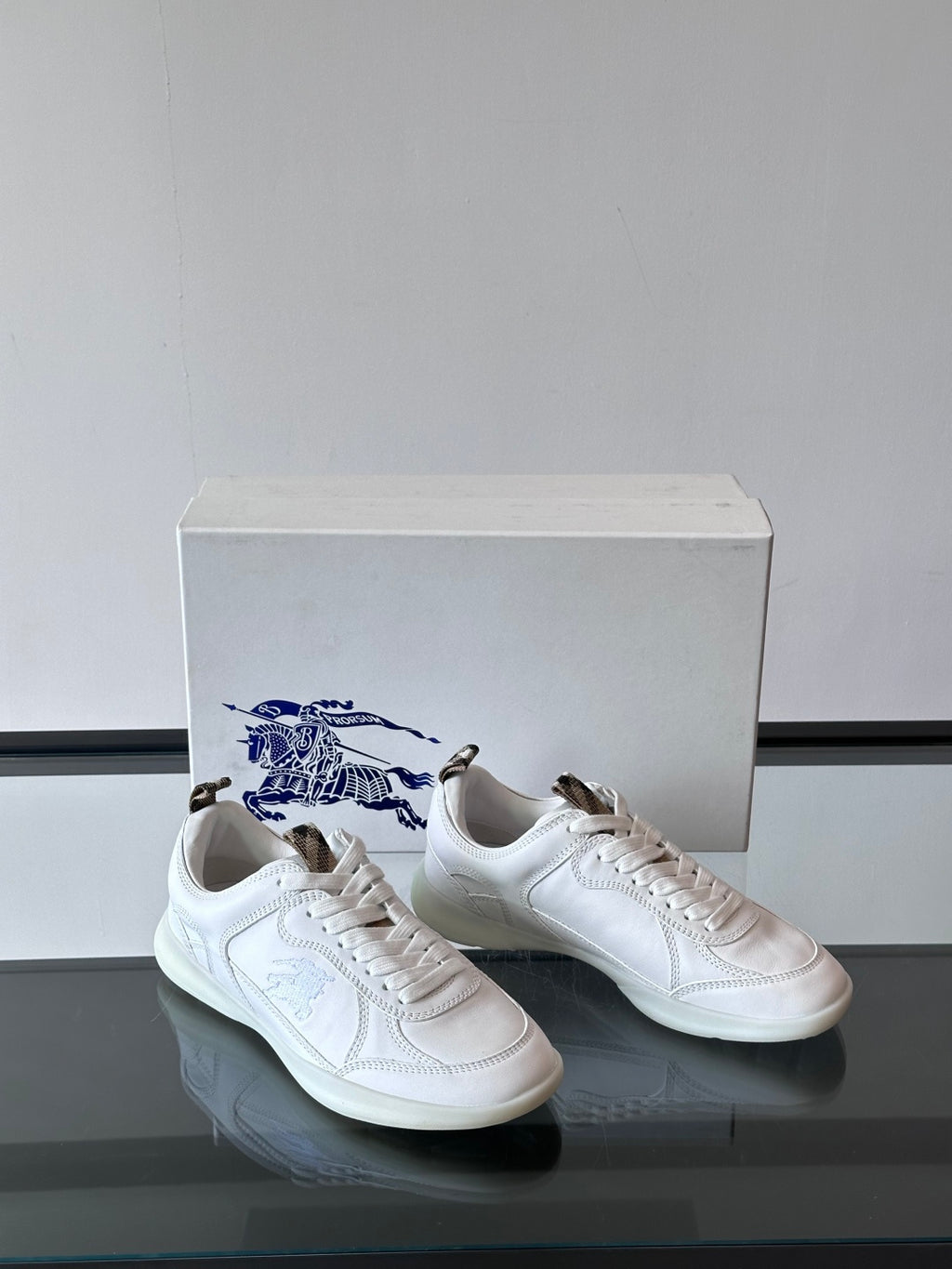 White low-top sneakers with blue logo embroidery, front/side angle on box
