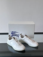 White low-top sneakers with blue logo embroidery, front/side angle on box