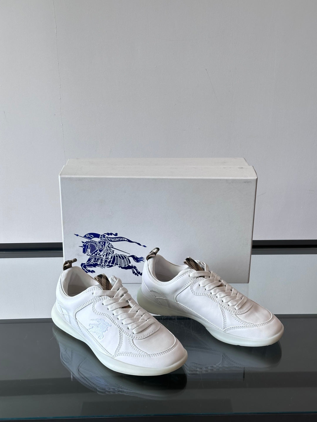 White low-top sneakers with blue logo embroidery, front/side angle on box