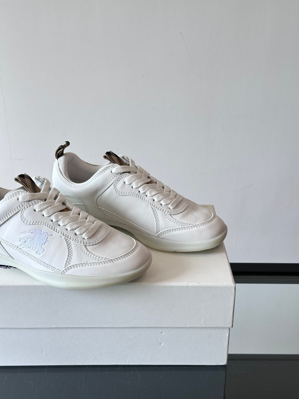 Two white low-top sneakers on box, close angled side views with blue logo