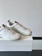 Two white low-top sneakers on box, close angled side views with blue logo