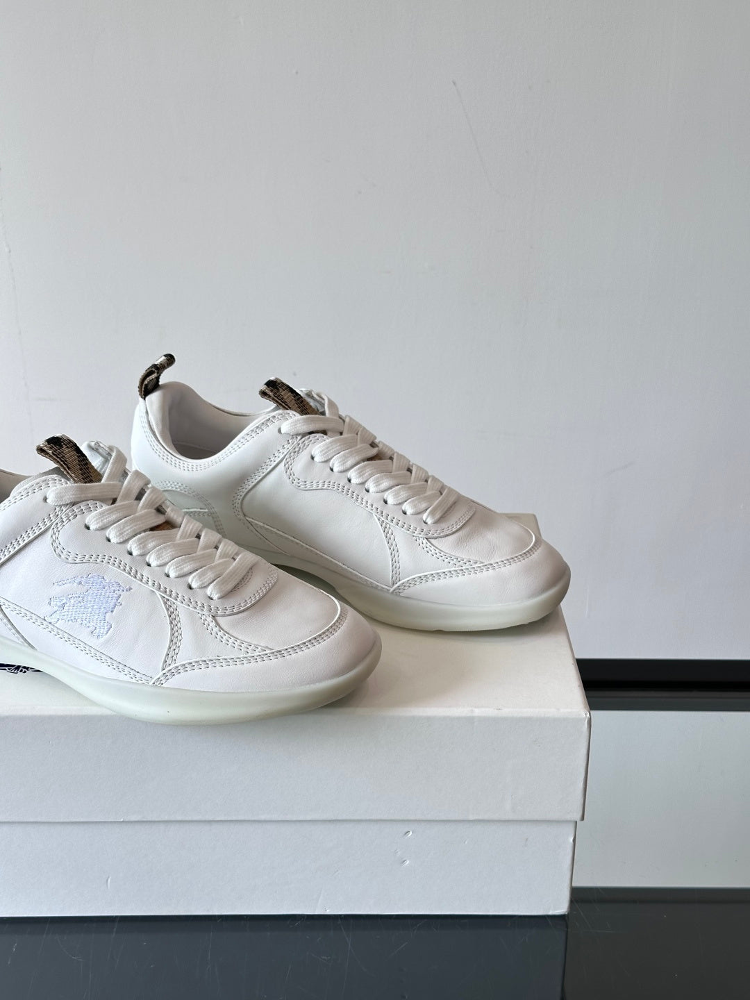 Two white low-top sneakers on box, close angled side views with blue logo