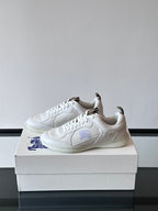 White low-top sneakers with laces and blue logo detail, angled side view