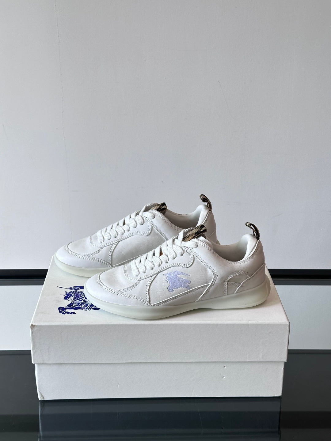 White low-top sneakers with laces and blue logo detail, angled side view