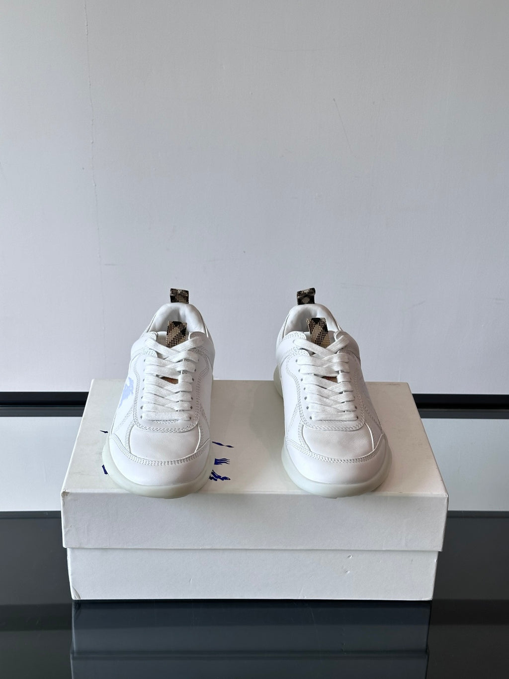 White low-top sneakers with laces and blue logo detail, rear quarter view