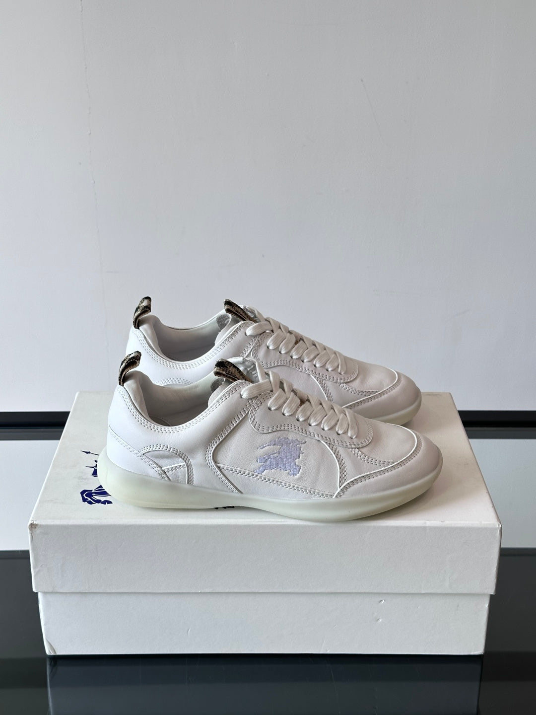 Pair of white low-top sneakers with blue logo embroidery on the sides
