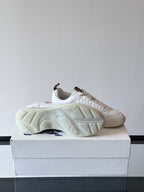 White low-top sneakers on box showing underside tread and blue logo