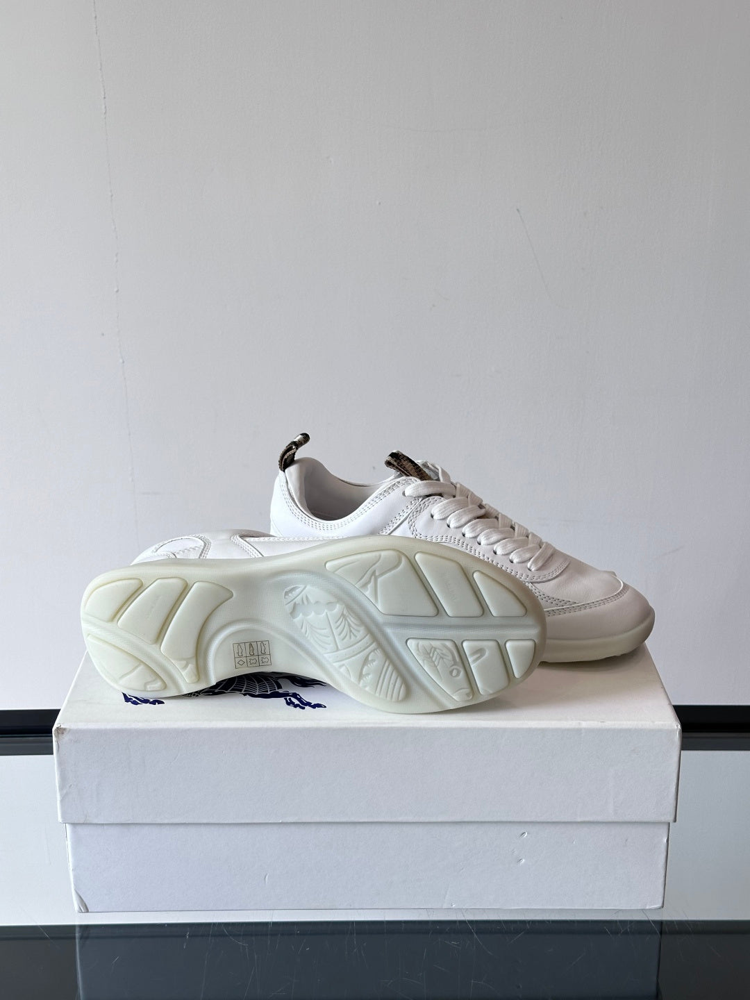White low-top sneakers on box showing underside tread and blue logo