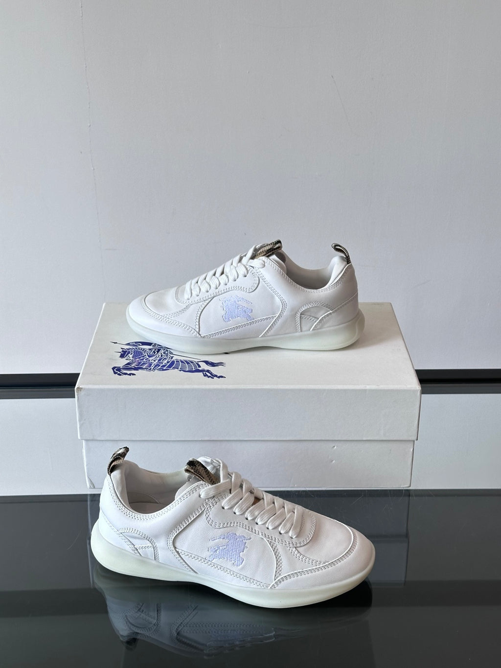 White low-top sneakers with blue logo embroidery, one side view on box