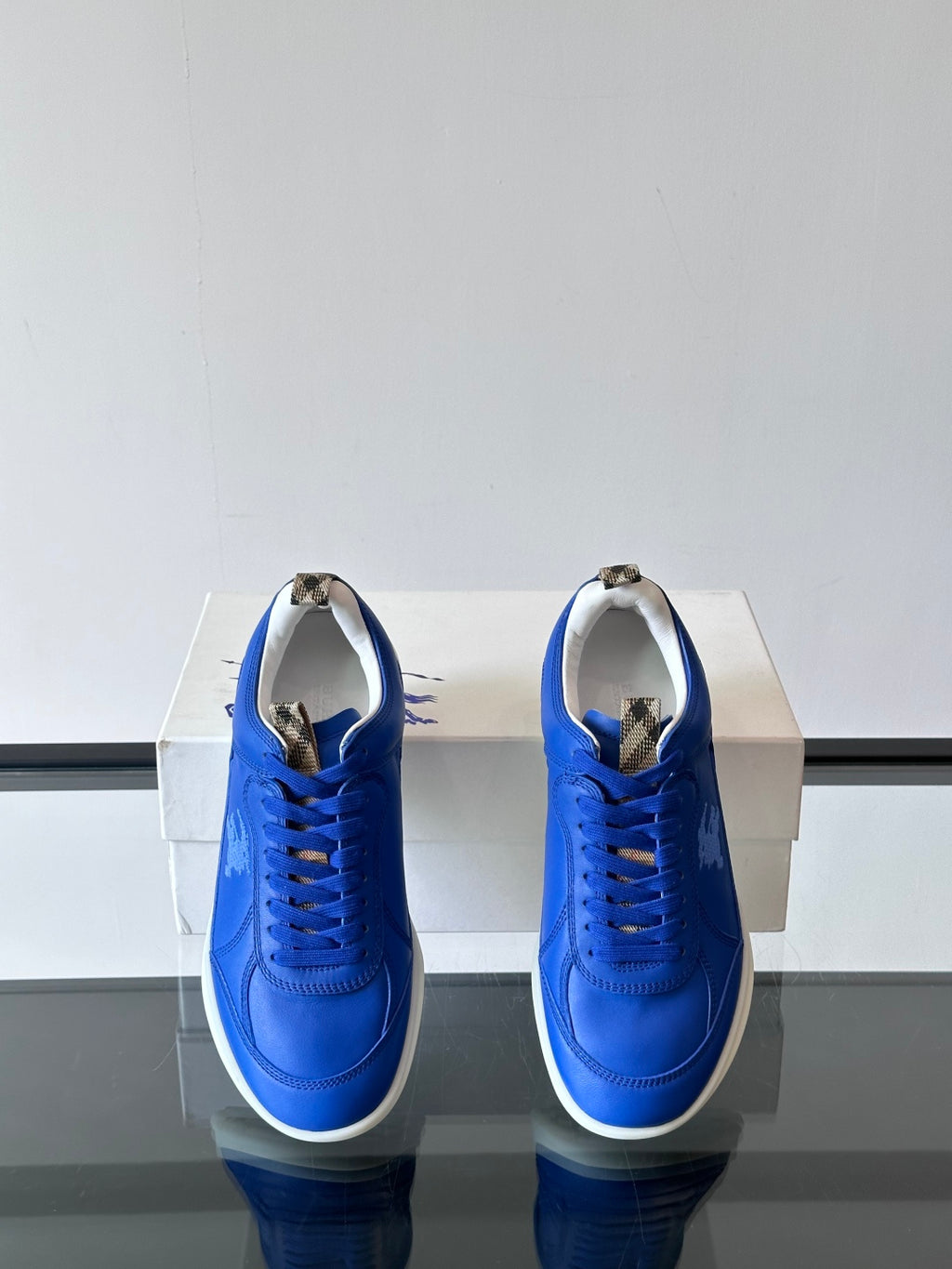 Blue lace-up sneakers with white soles, rear view pair on a box