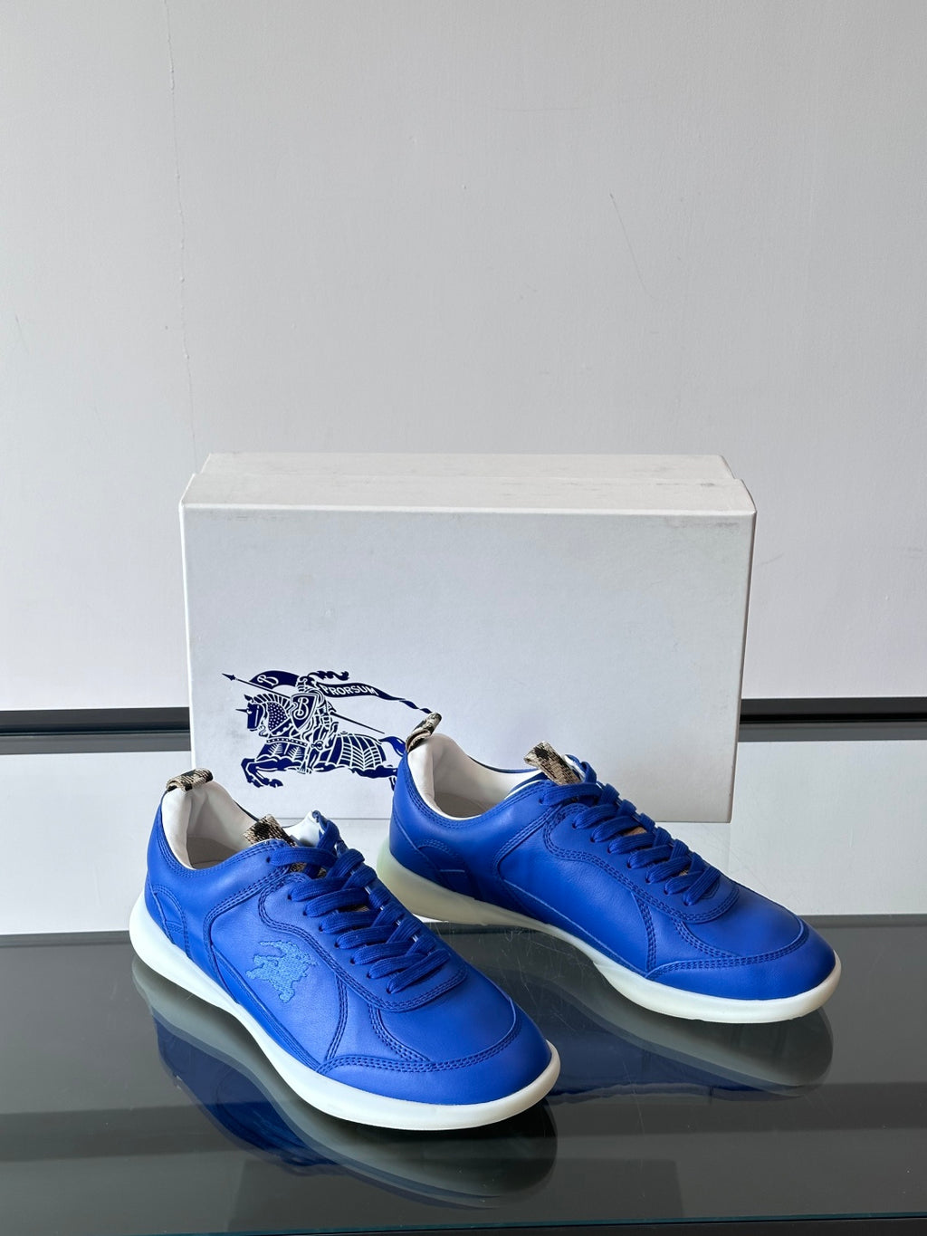 Blue lace-up sneakers with white soles, front view pair on a box