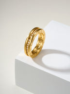 Gold ring with gemstone details and engraved markings, standing on a pedestal