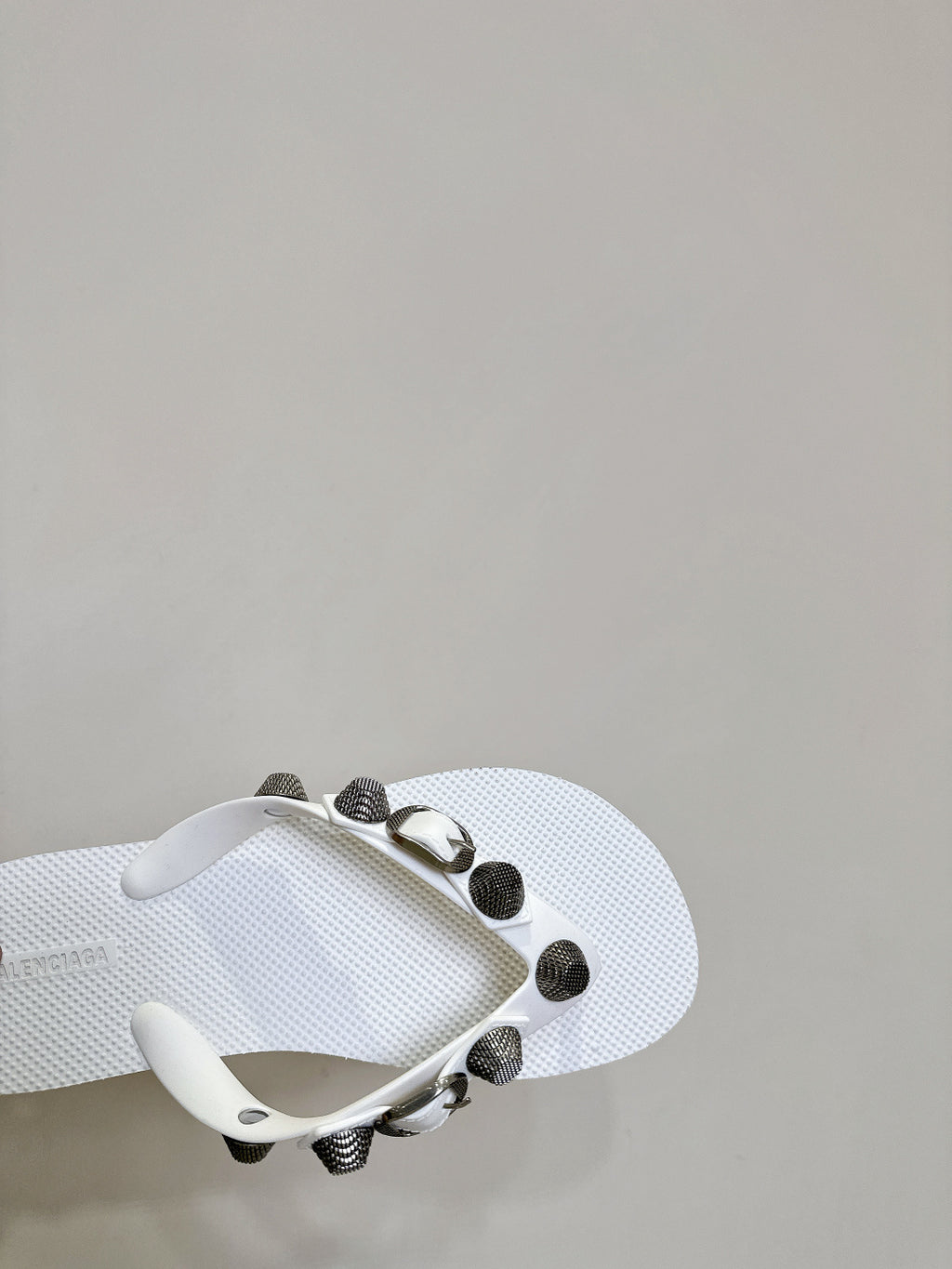 White thong sandals with studded oval hardware on the strap, angled side close-up.