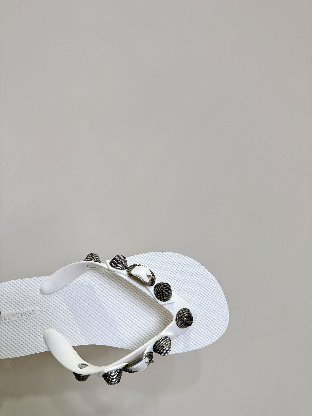 White thong sandals with studded oval hardware on the strap, angled side close-up.