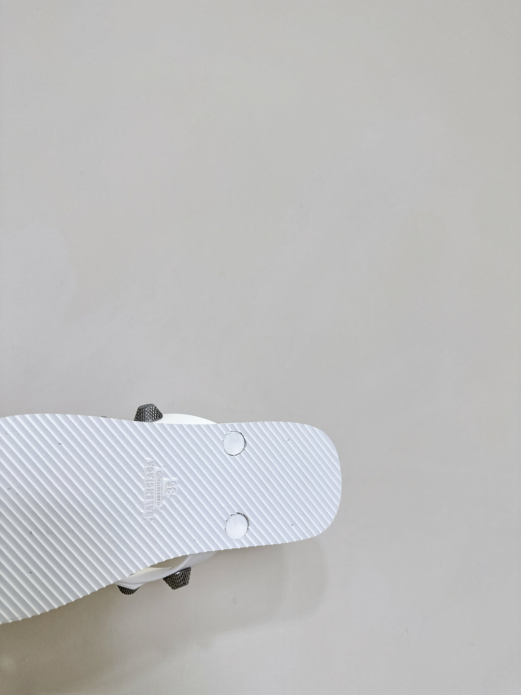 White sandal outsole close-up with tread pattern and small stud details underfoot.