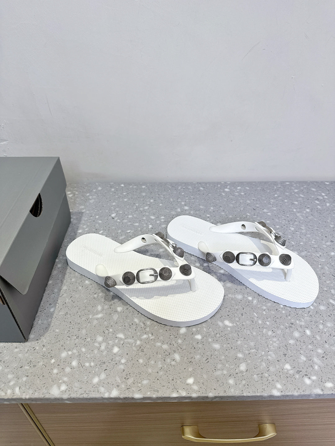 White thong sandals with studded strap hardware, angled side view of both shoes.
