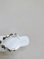 White thong sandals, close side view of the footbed and studded strap hardware.