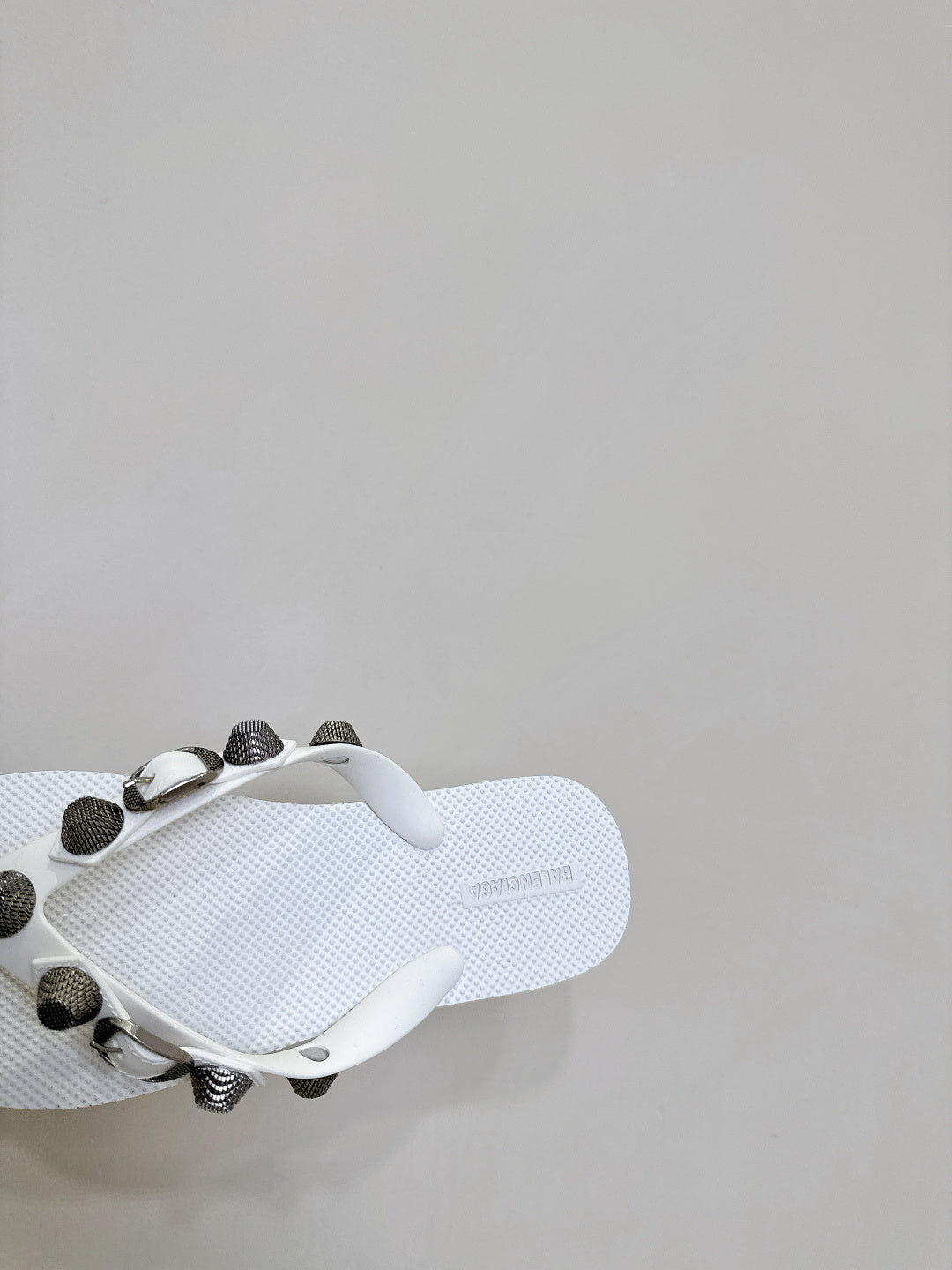 White thong sandals, close side view of the footbed and studded strap hardware.