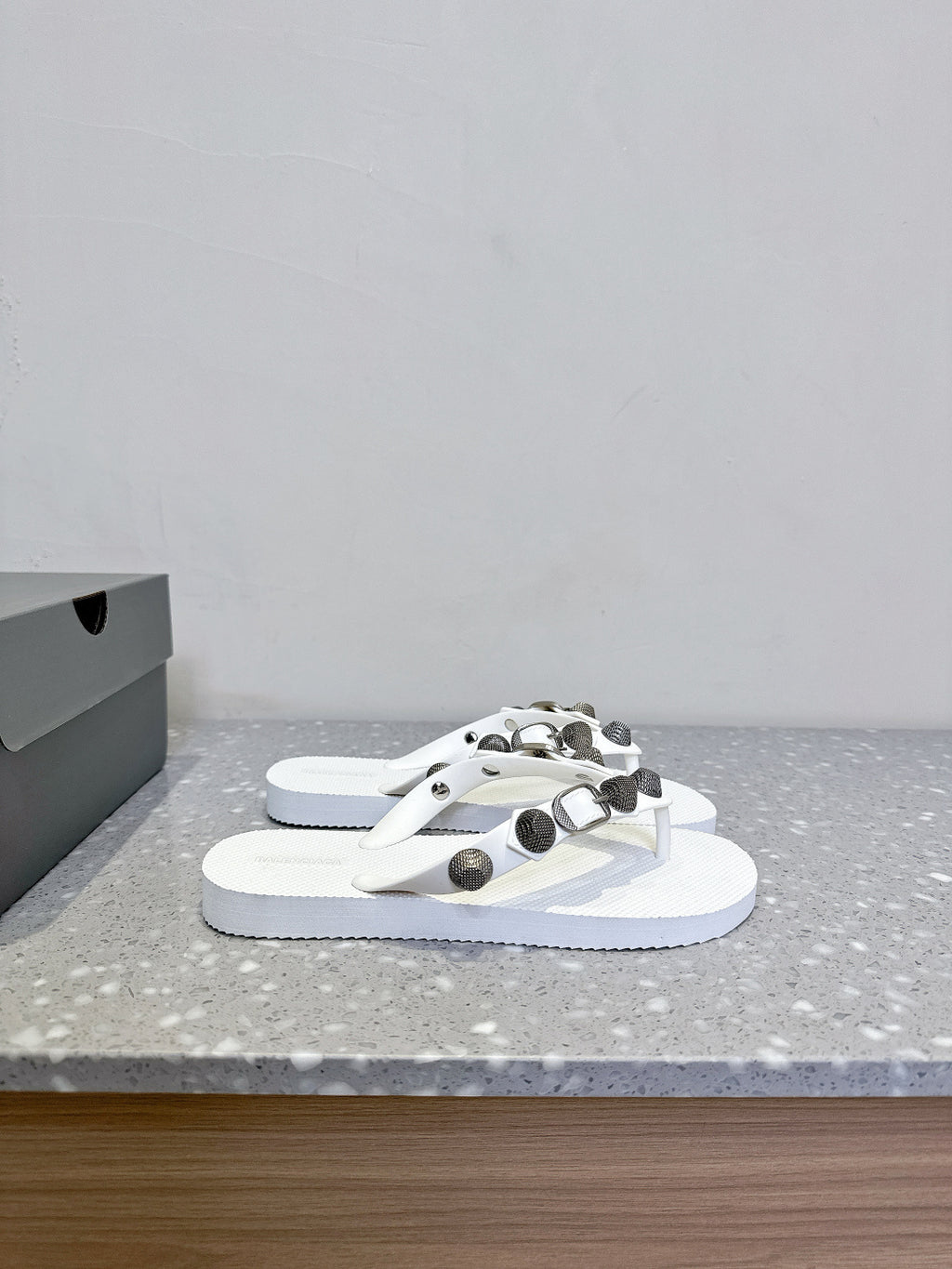 White thong sandals with studded oval hardware straps, front view of the pair.