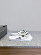 White thong sandals with studded oval hardware straps, front view of the pair.
