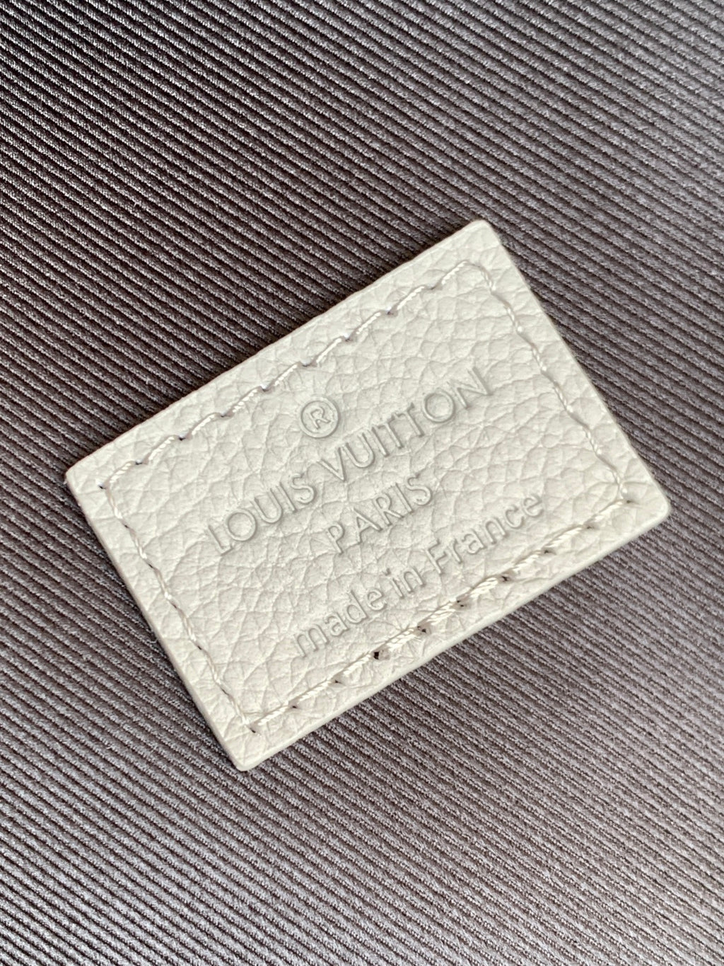 Louis Vuitton authenticity tag with debossed logo on light leather