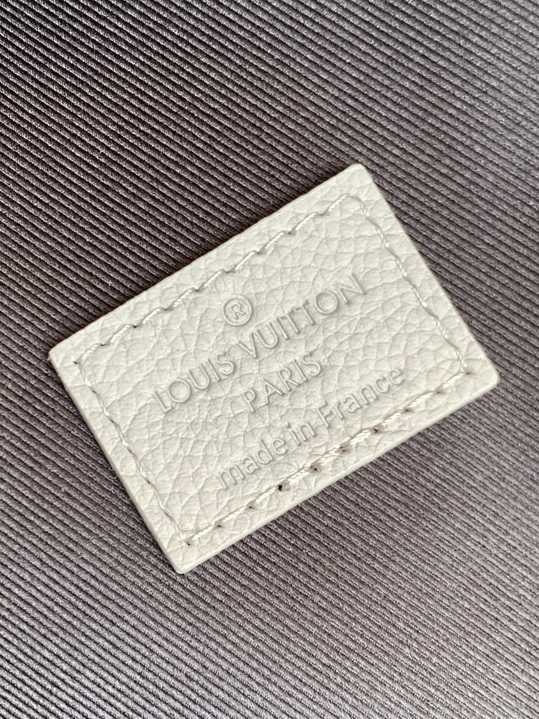 Louis Vuitton authenticity tag with debossed logo on light leather