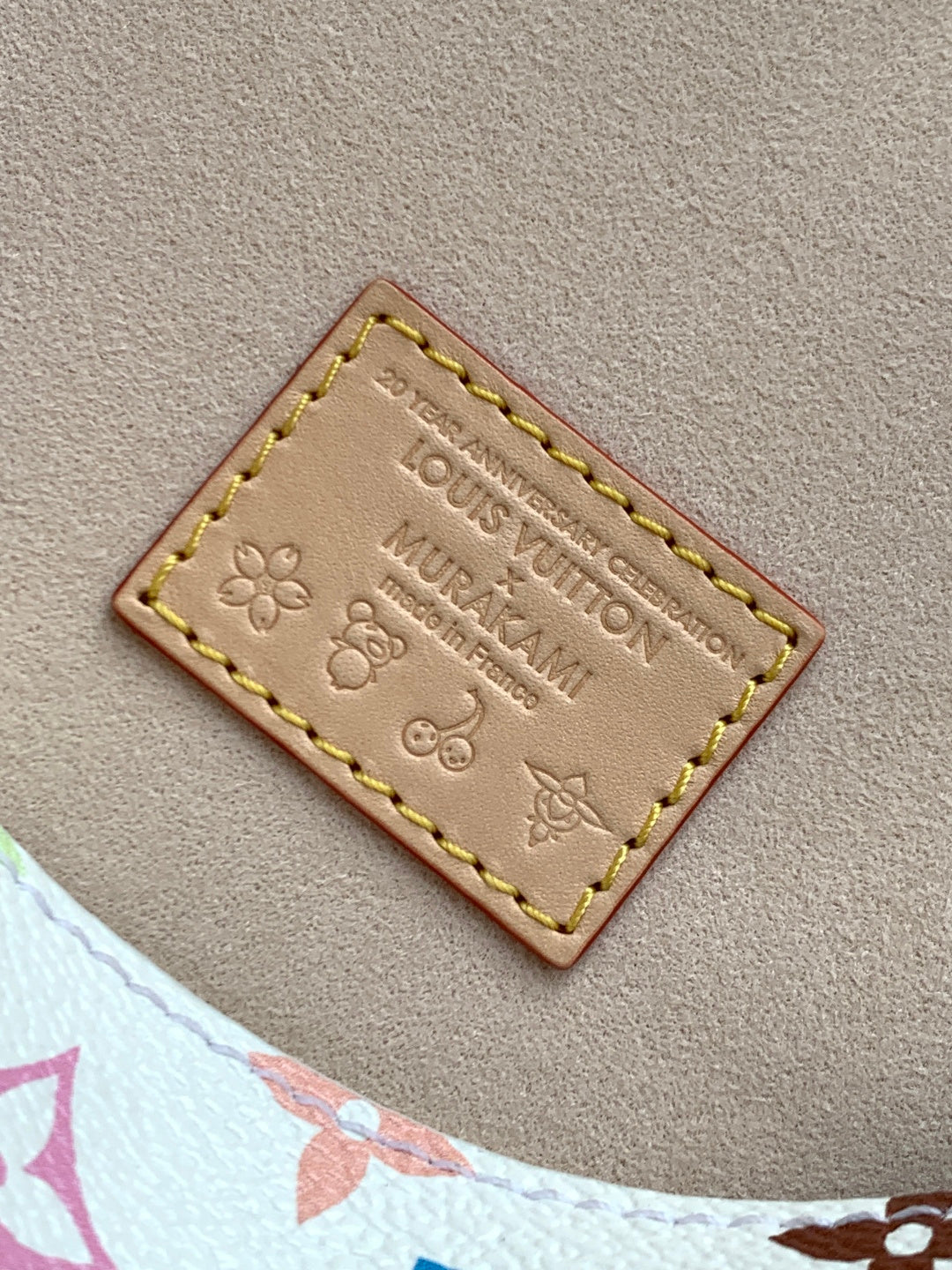 Brown leather label patch with Louis Vuitton embossing and yellow/gold stitching.