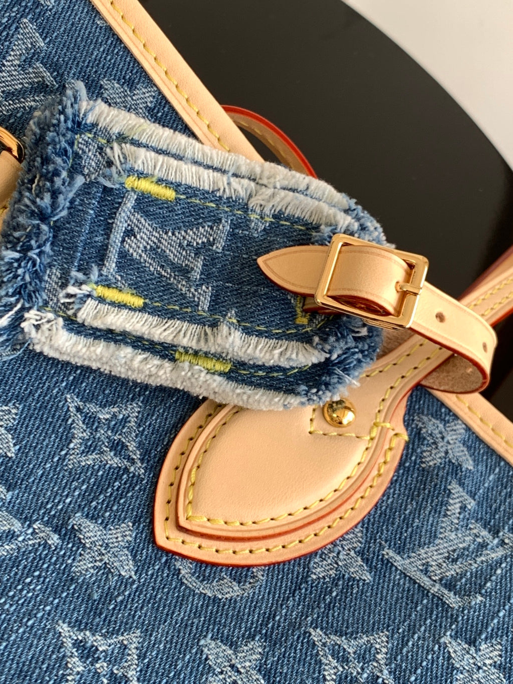 Blue monogram tote bag close-up: tan tab, buckle, and stitched edge