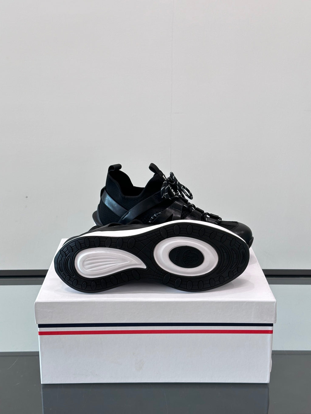 Black Moncler sneaker outsole view on box, with circular tread pattern and laces.